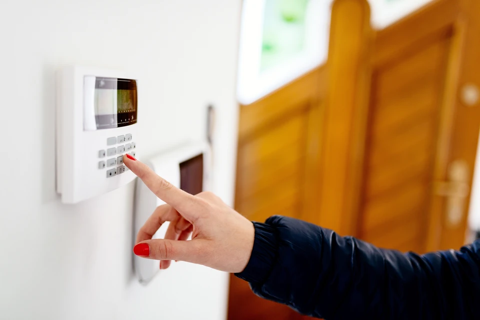 Une personne utilise un panneau de contrôle d'alarme domestique monté sur un mur jaune intérieur